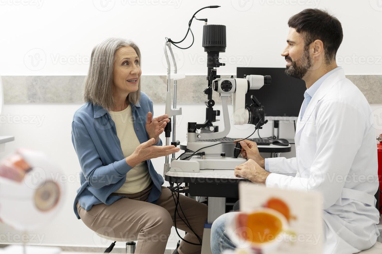 Senior woman discussing eye health with optometrist using phoropter in ophthalmology clinic photo