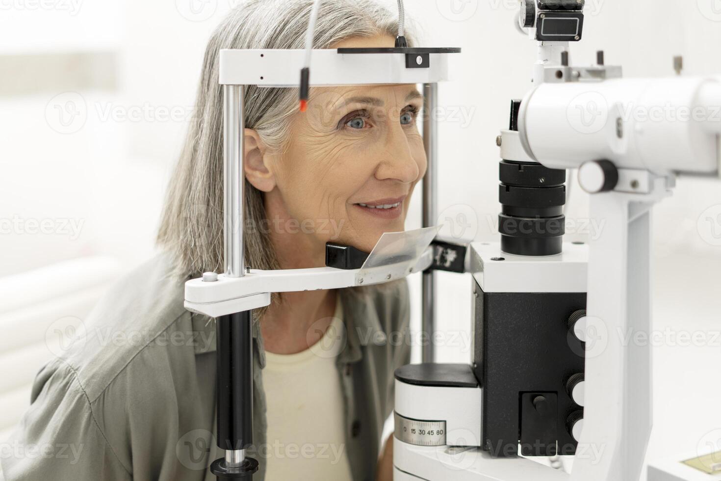 Senior woman undergoing eye exam using phoropter in ophthalmology clinic photo