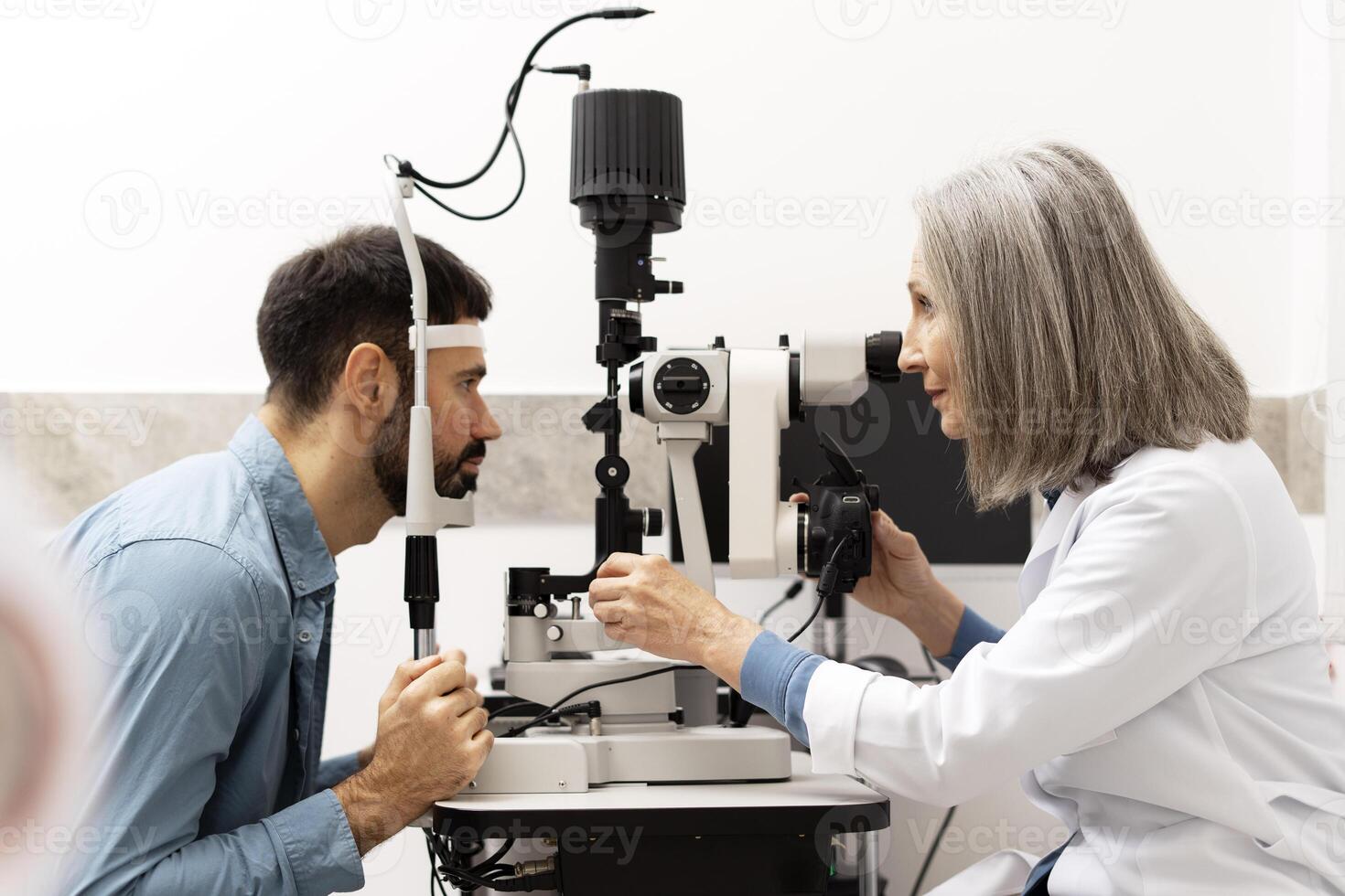 Senior female doctor performing eye exam on male patient using medical equipment photo