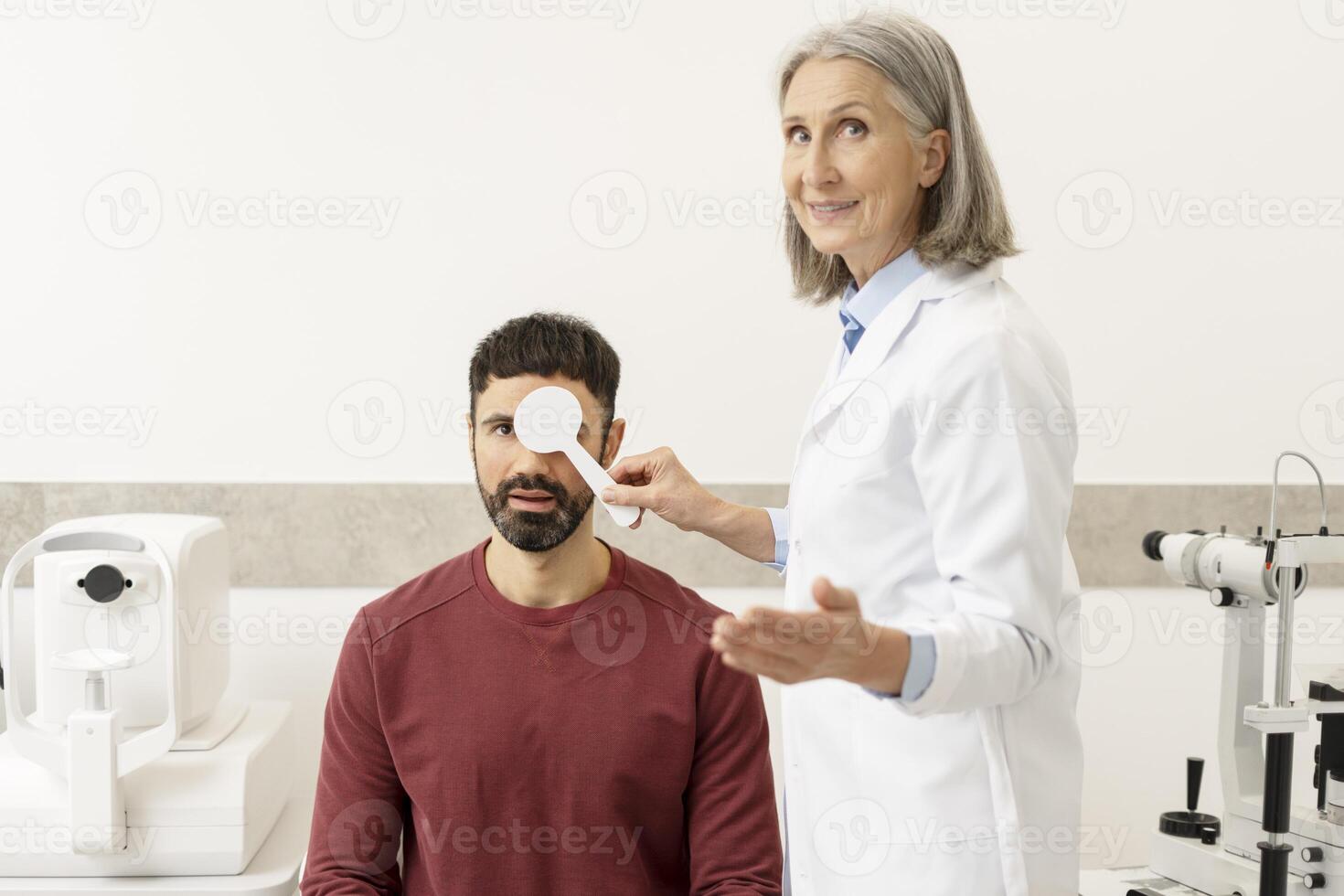 Senior female doctor performing eye exam on male patient in ophthalmology clinic photo