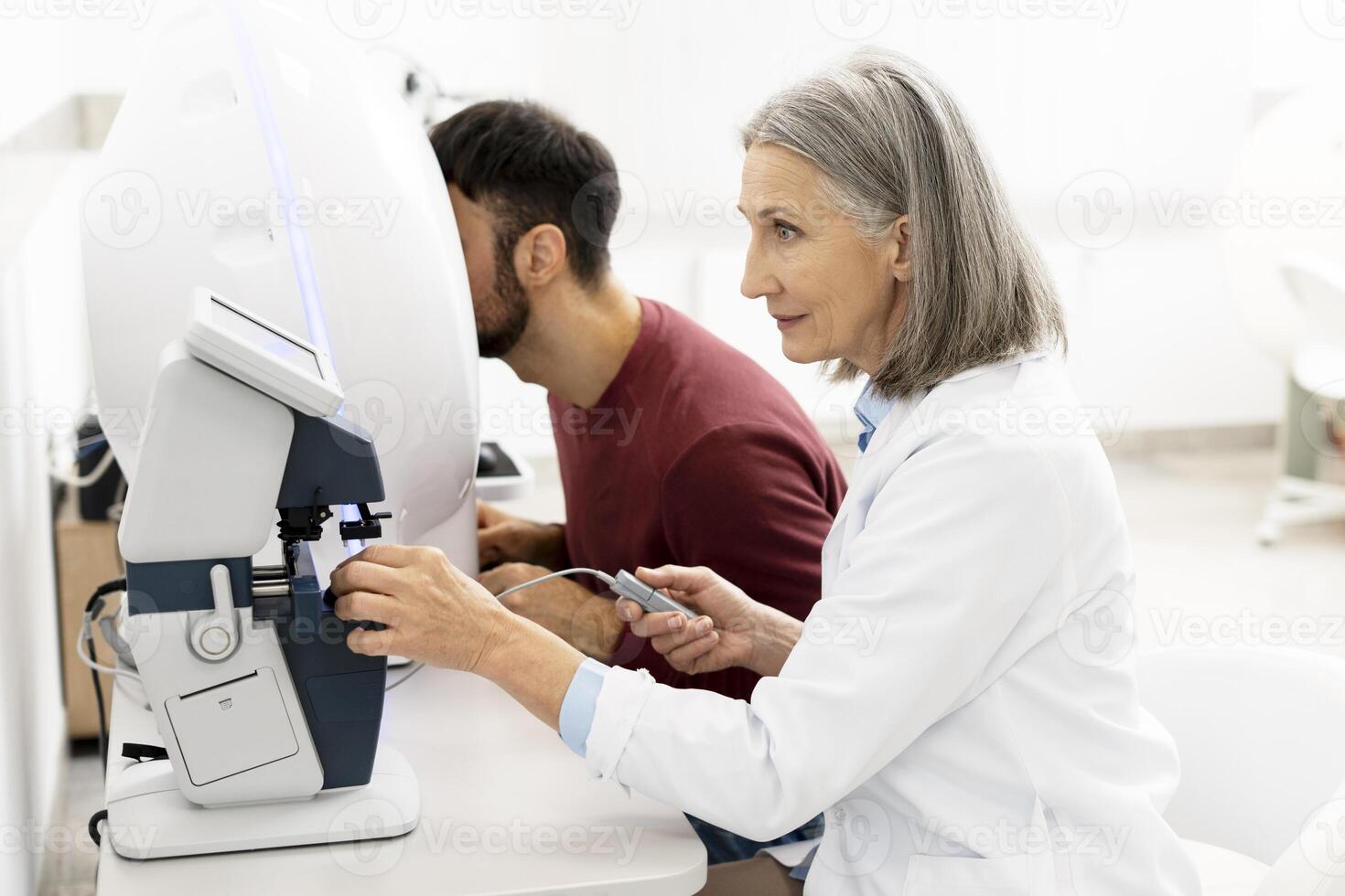 Senior female doctor performing eye exam on male patient using modern equipment photo