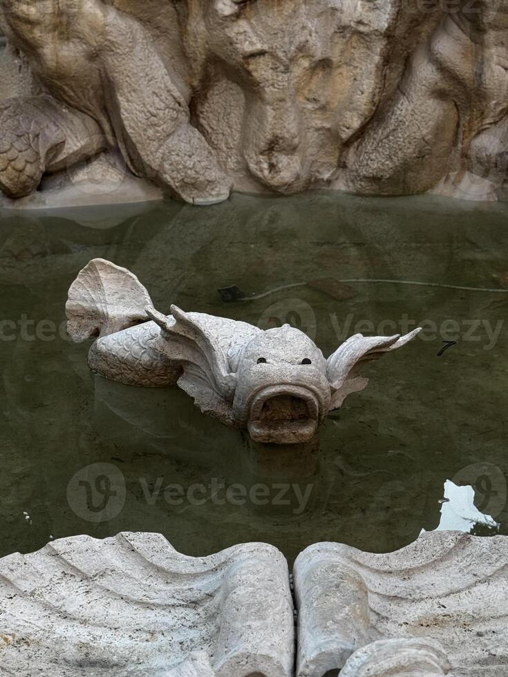 A beautifully crafted stone fish sculpture rests serenely in calm waters, encircled by intricate artistic stonework within a historic courtyard photo