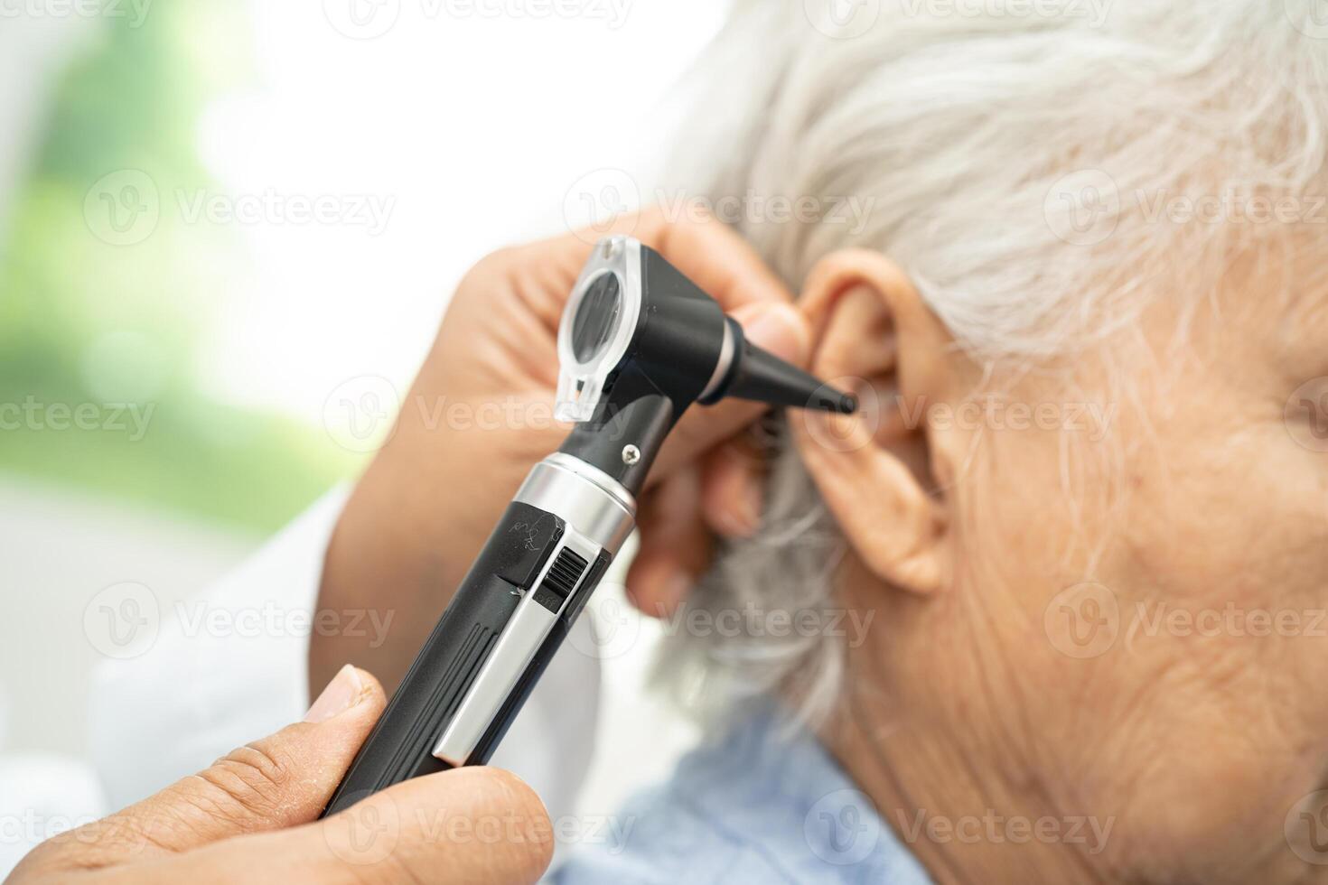 Audiologist or ENT doctor use otoscope checking ear of asian senior woman patient treating hearing loss problem. photo