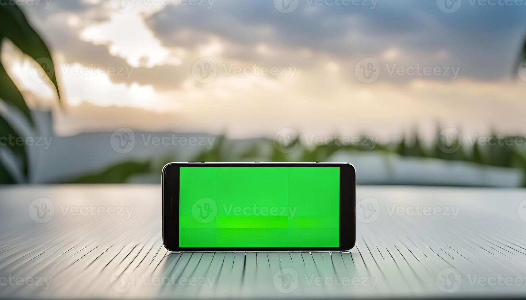 Smartphone with Green Screen on a Table with Blurred Sunset Background photo