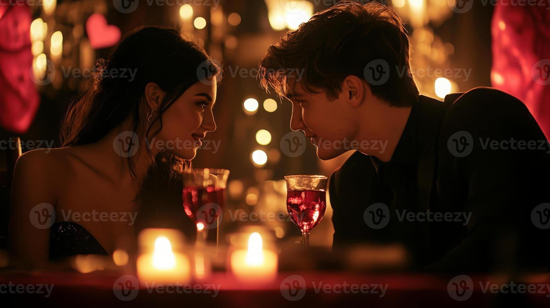 Two young individuals are seated at a beautifully decorated table filled with candles and soft lighting. Their eyes lock as they share a tender moment over drinks, creating an intimate atmosphere. photo