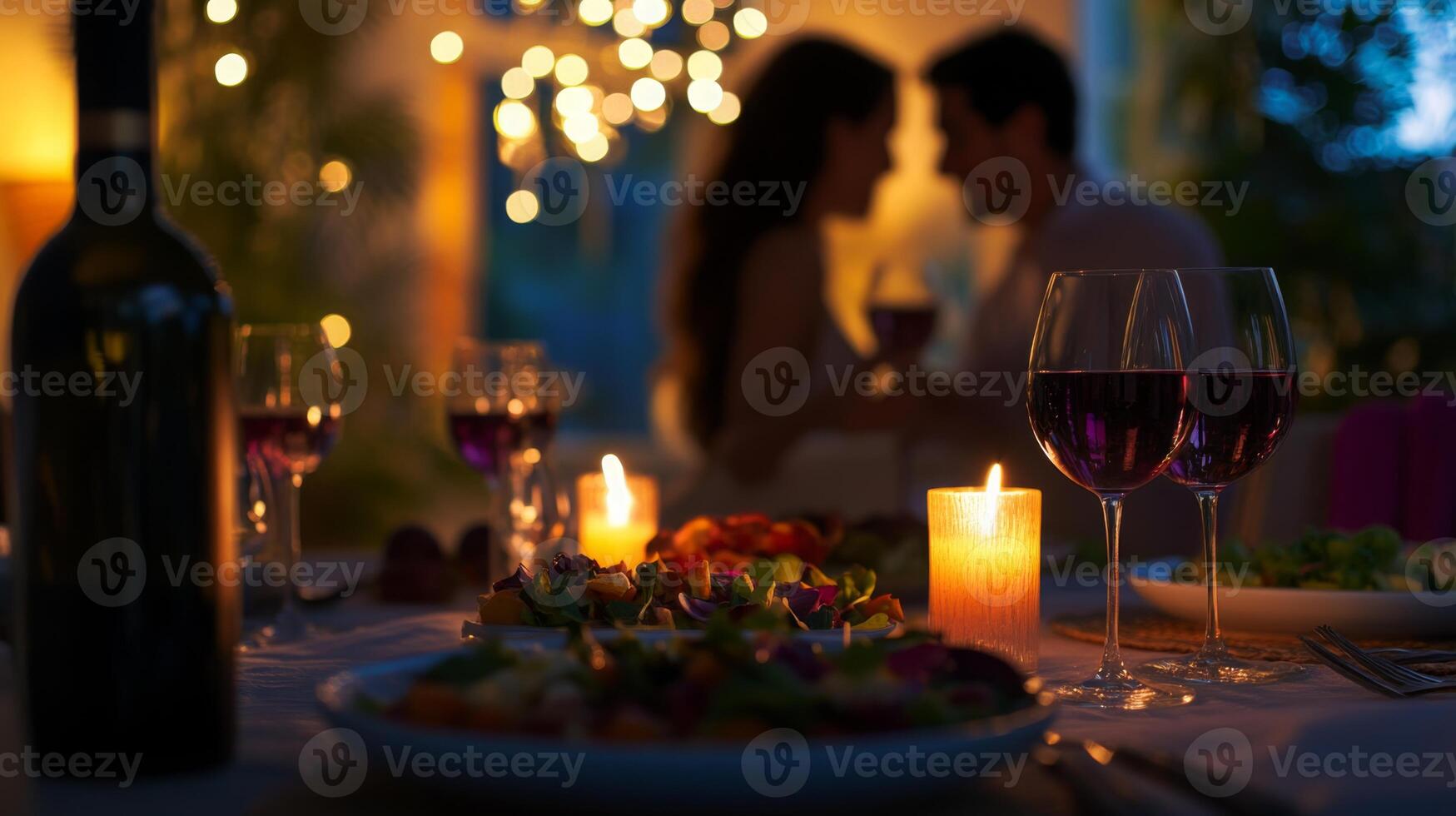 A couple enjoys a romantic dinner, surrounded by soft candlelight and decorative string lights. Tables are set with delicious food and glasses of red wine, creating an intimate atmosphere. photo