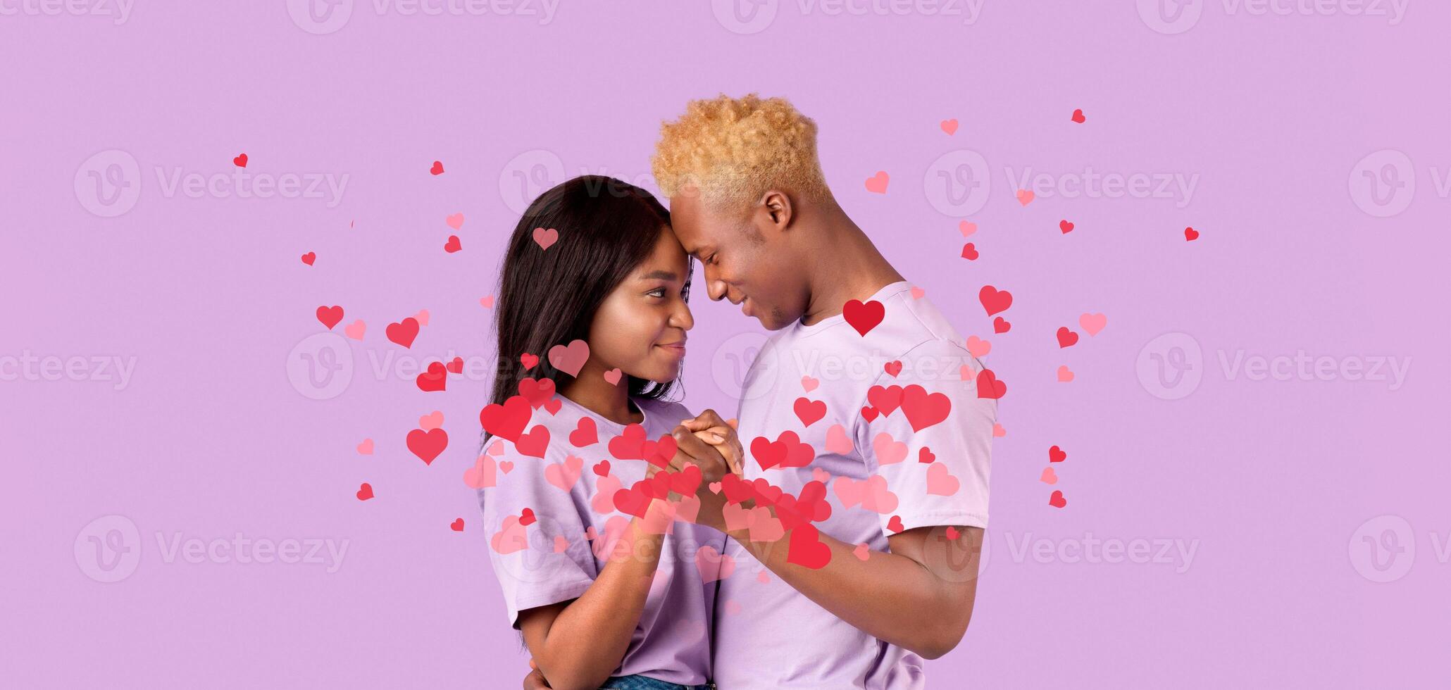 A loving black couple celebrates their bond with a kiss, surrounded by floating hearts. This sweet moment captures their affection on a special occasion filled with joy and romance. photo