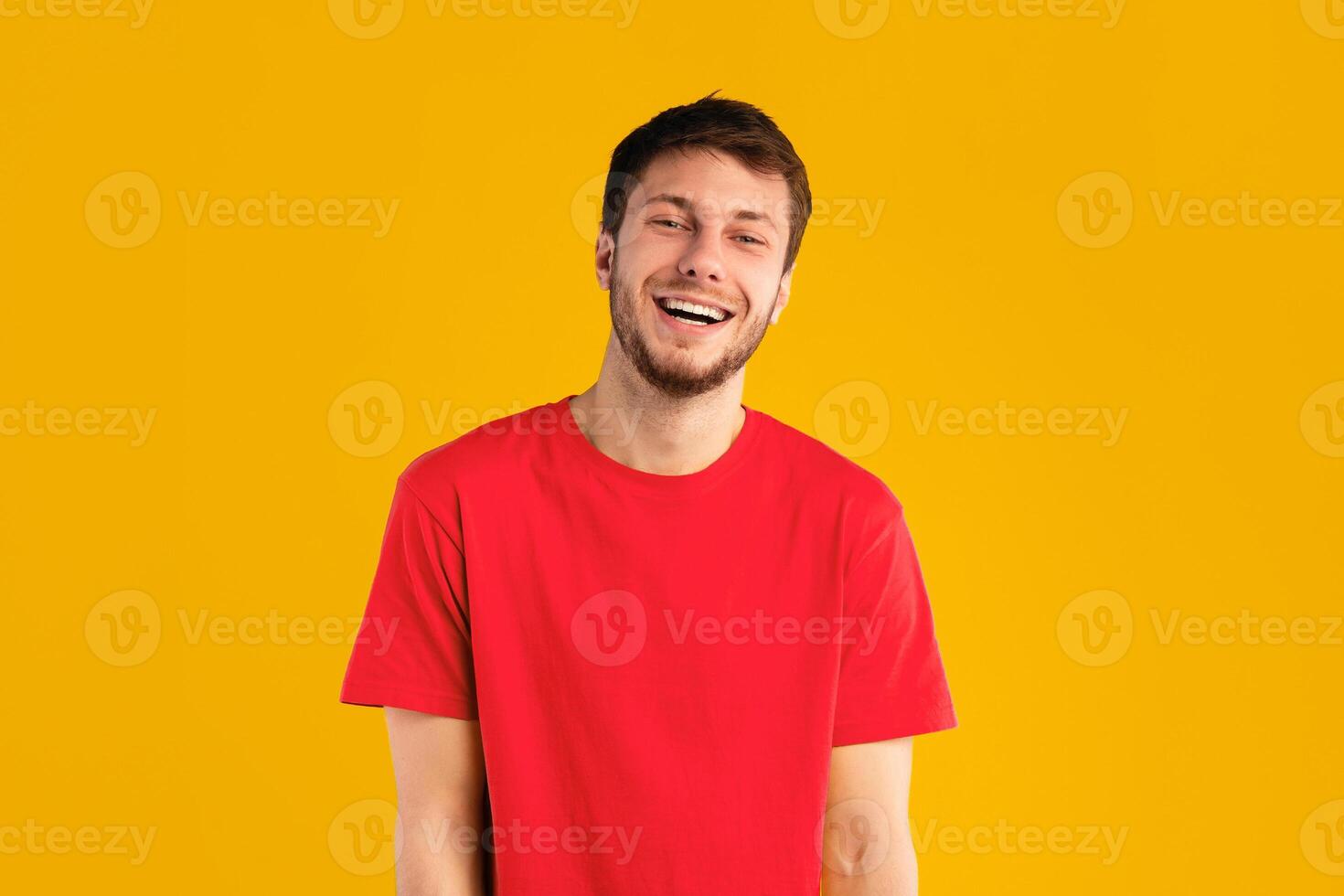 Portrait of handsome guy smiling and looking at camera over blue studio background. Happy caucasian man with shy facial expression posing, male student model showing positive emotions and laughing photo