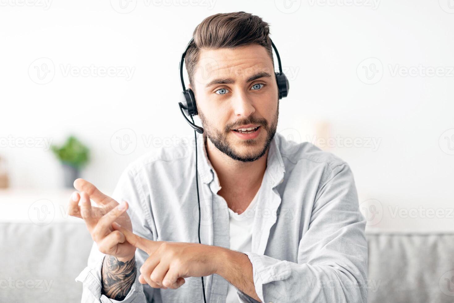 Remote job and online meeting. Serious man having web conference, wearing headset and gesturing to laptop camera, working at home, sitting on couch photo
