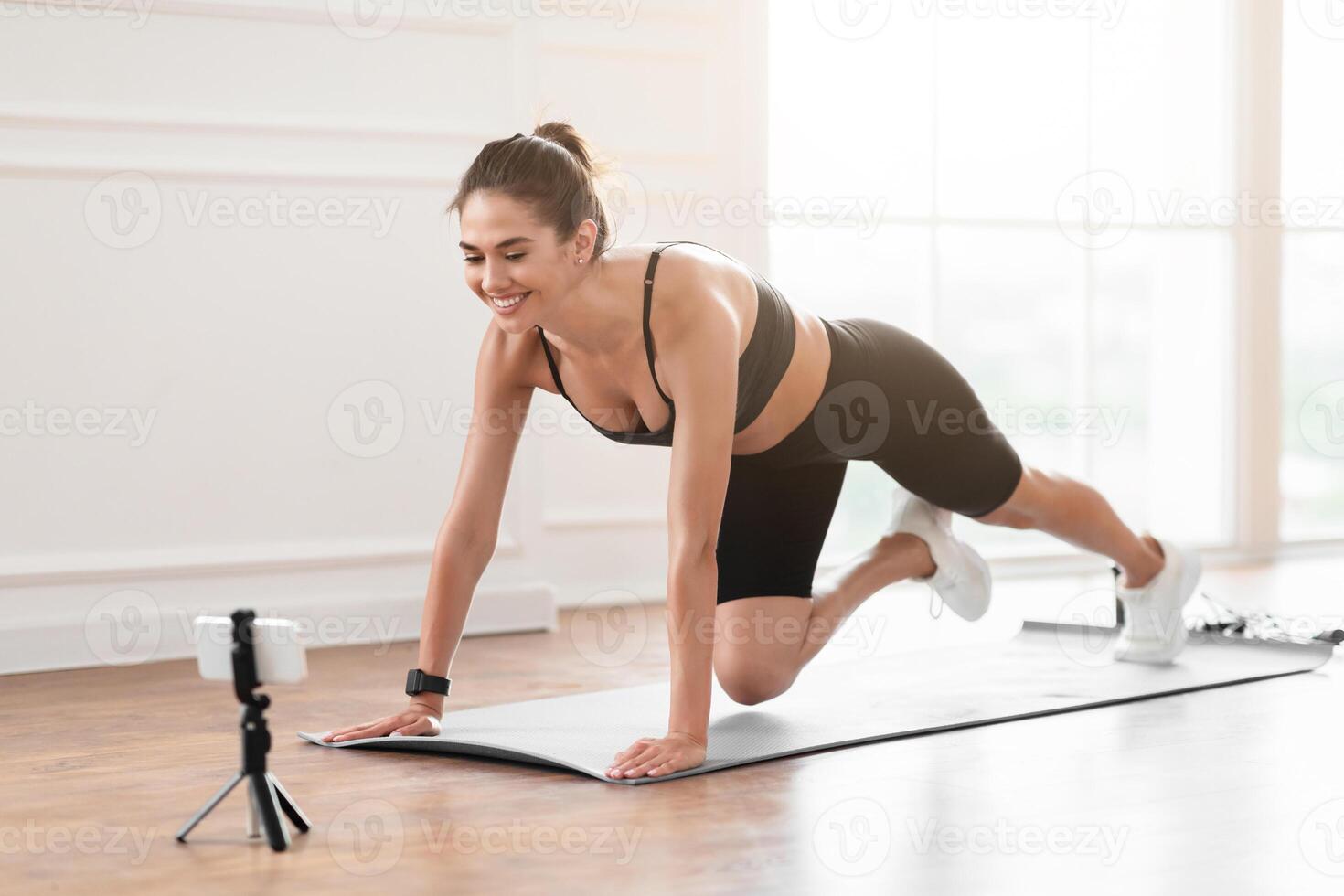 Smiling Lady Training At Home In Front Of Cellphone On Tripod, Beautiful Female Fitness Blogger Shooting Tutorials, Doing Cross Body Mountain Climbers Exercise At Camera Having Call With Trainer photo