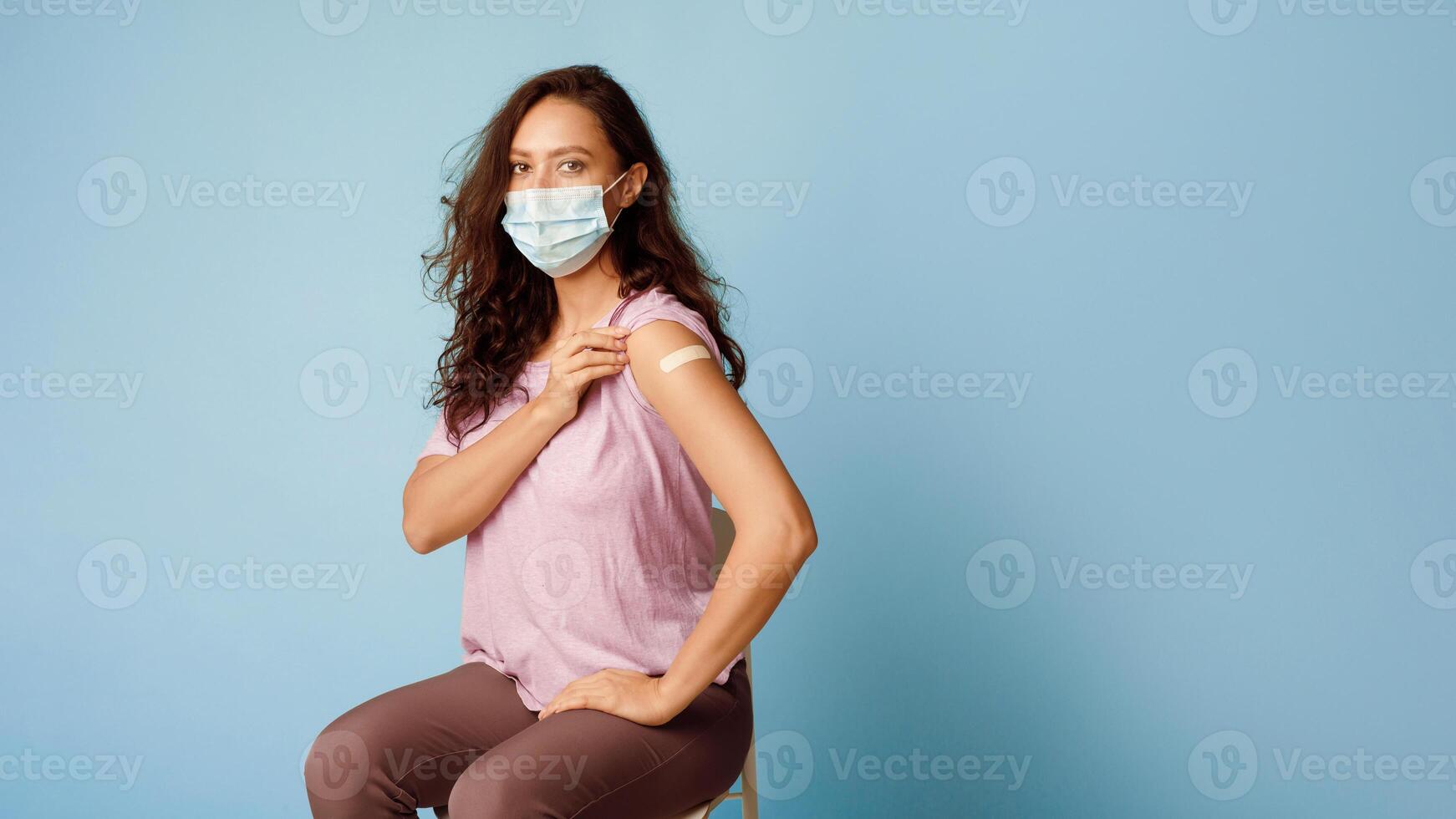 Covid-19 Vaccination. Vaccinated Lady Showing Arm After Coronavirus Antiviral Vaccine Injection Sitting Over Blue Background, Wearing Face Mask. Corona Virus Prevention. Panorama, Empty Space photo