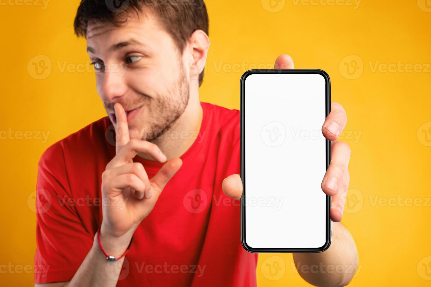 Man with white blank cellphone screen holding index finger on lips, showing gesture of secret, empty space, mock up photo