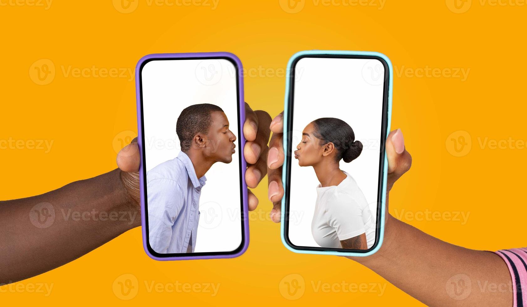 Two individuals hold smartphones, each displaying the other face as they share a playful kiss gesture. The bright yellow background enhances the warm, loving atmosphere of their connection. photo