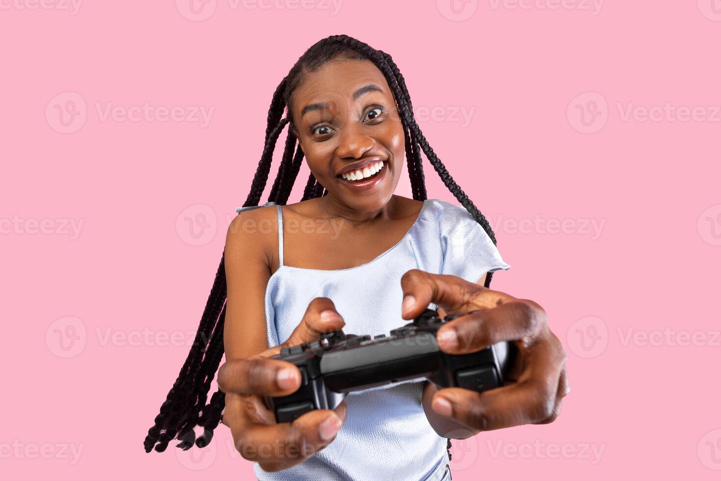 Millennial black lady with joystick playing exciting game on pink studio background. Happy young woman with afro bunches holding controller, participating in online gaming championship photo