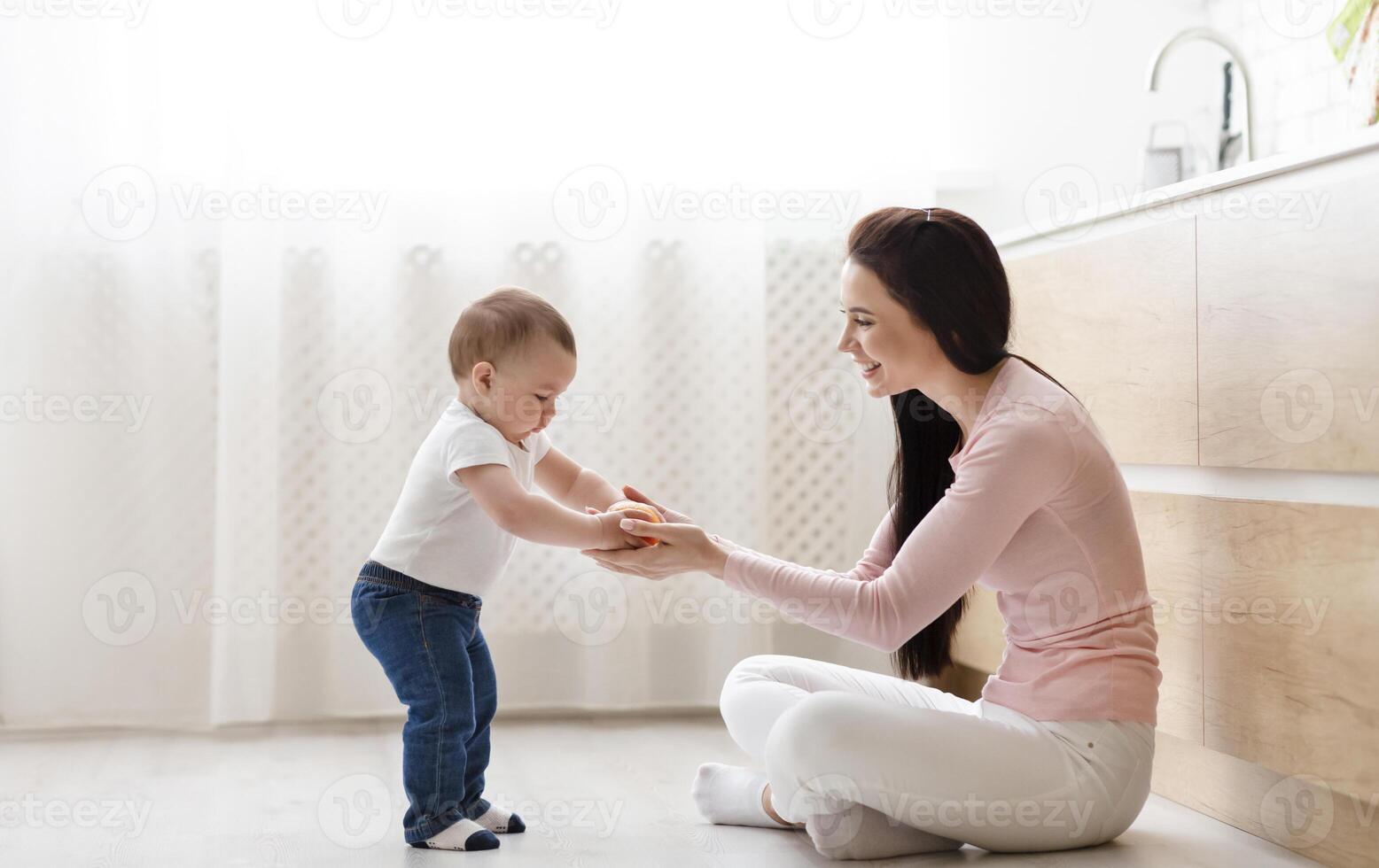 Right parenting. Mother playing with toddler on kitchen floor, studying vegetables, empty space photo