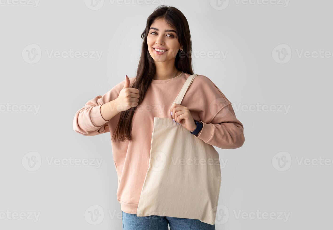 Zero Waste. Millennial Woman Showing Blank Eco Bag And Gesturing Thumbs Up Posing Standing On White Studio Background, Smiling To Camera. I Like Ecology Friendly Lifestyle, No More Plastic Concept photo
