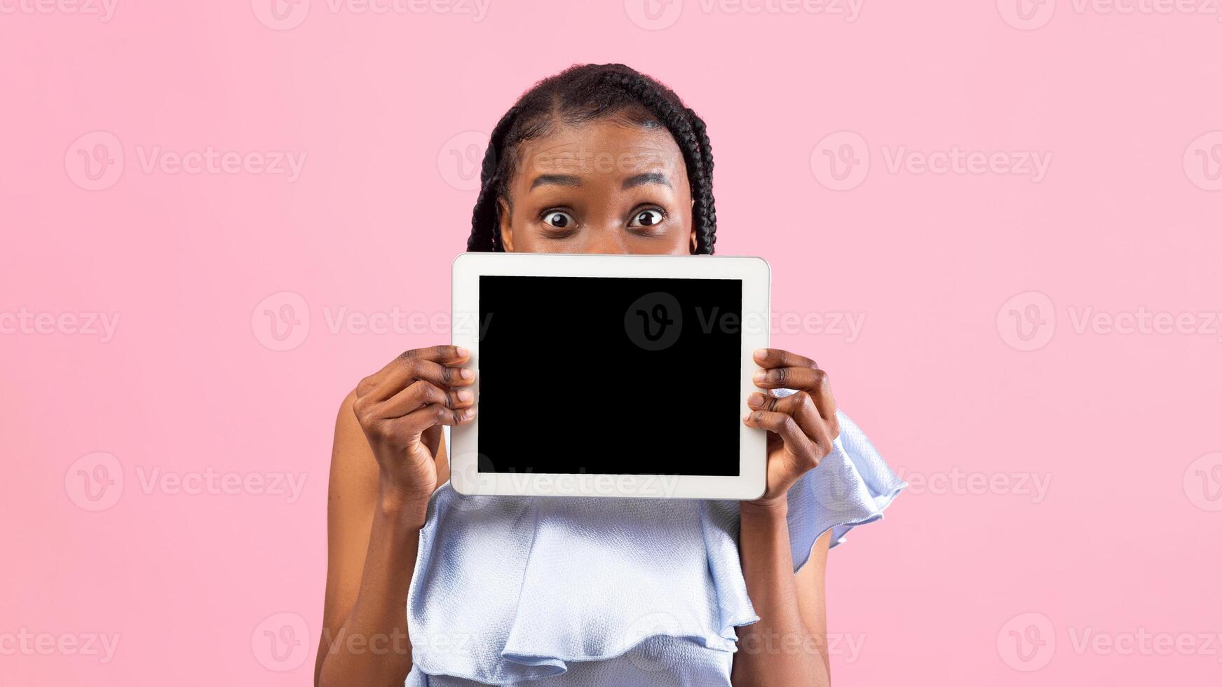 Millennial African American lady hiding behind tablet pc with blank screen on pink studio background, mockup for app or website. Online life, education, communication concept photo