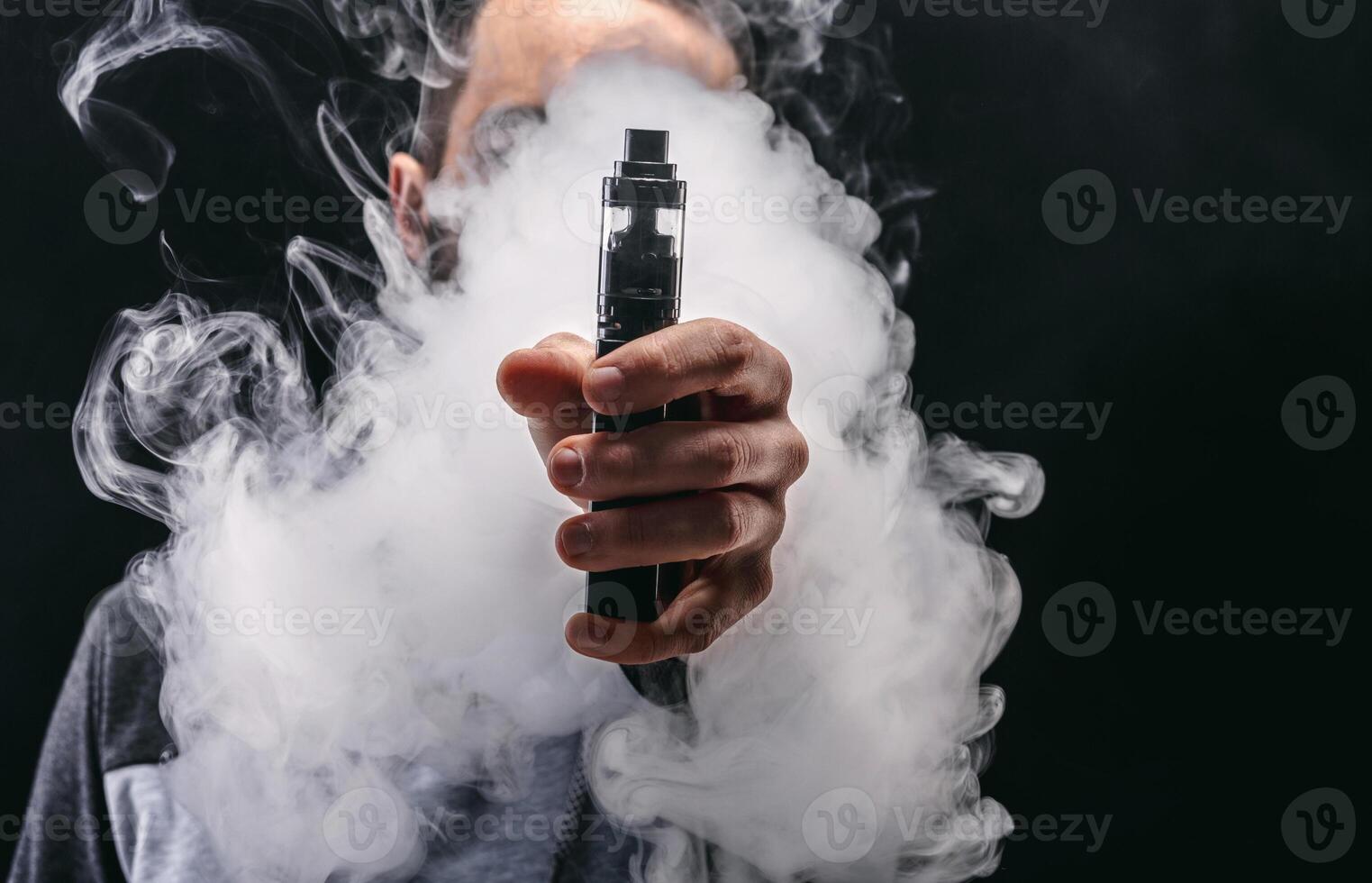Unrecognizable man in the cloud of vape smoke. Guy smoking e-cigarette to quit tobacco. Vapor and alternative nicotine free smoking concept, copy space photo