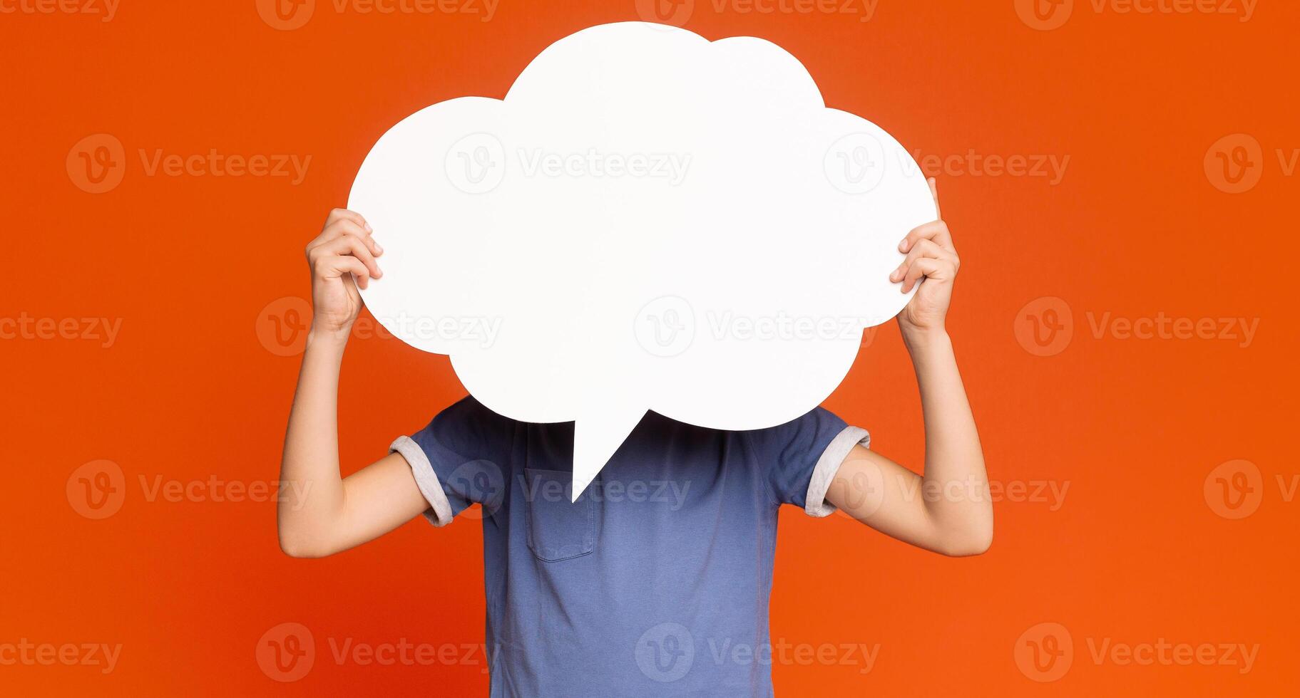 Little boy holding an empty speech bubble in front of his head, orange studio background, free space photo