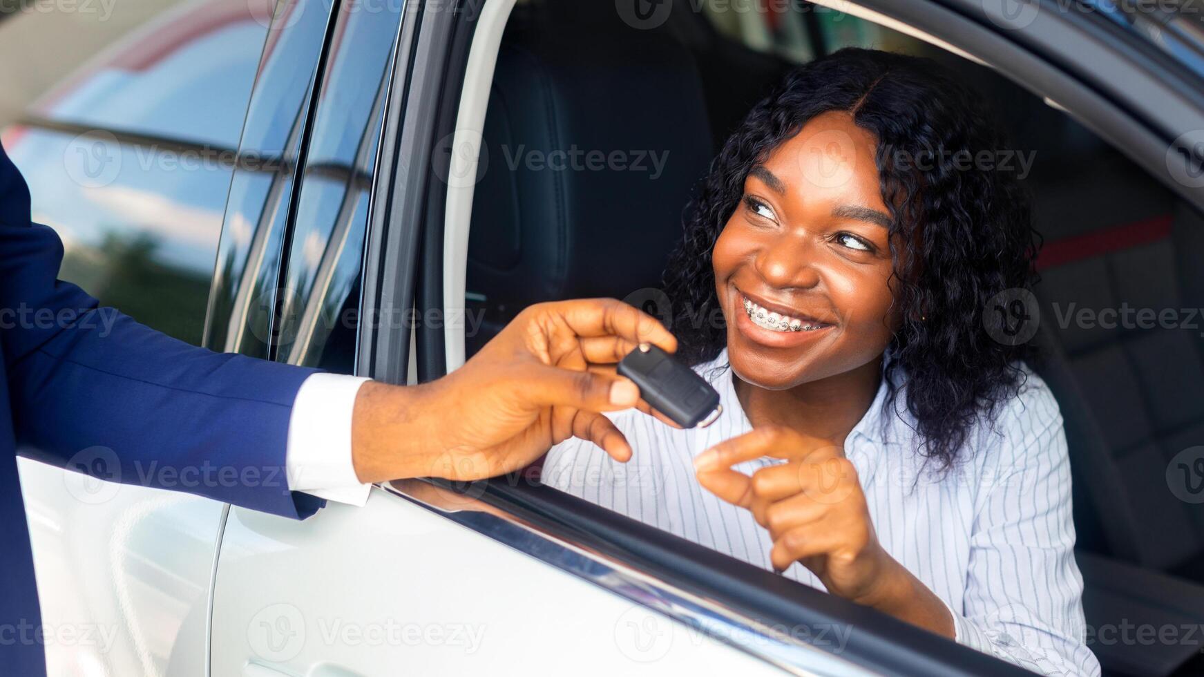 Happy Black Woman Sitting Inside Of Car And Taking Key From Salesman After Buying New Automobile In Dealership Center, Cheerful African American Female Customer Smiling Through Window, Closeup Shot photo