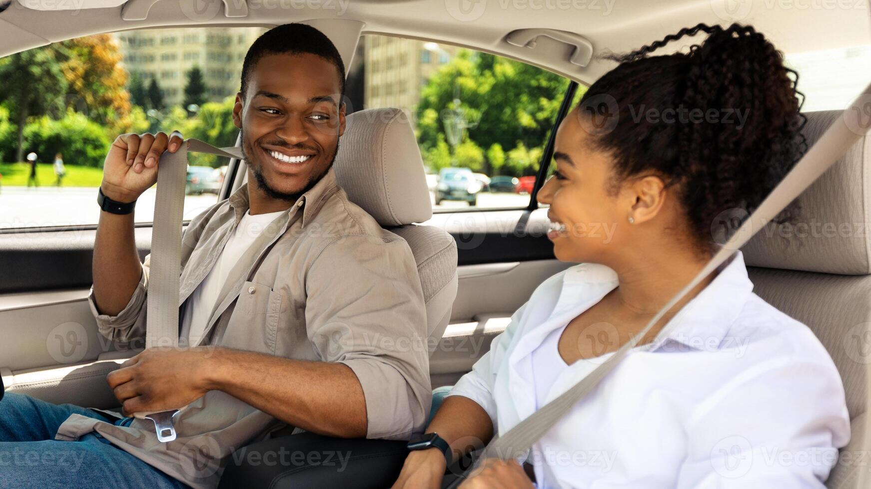 Happy African American Couple Sitting In Car Putting On Seat Belts Driving Automobile Having A Ride In City Outdoors. New Auto, Summer Travel Concept. Selective Focus photo