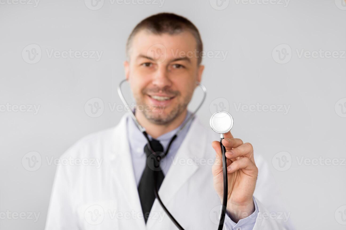 Portrait of professional male doctor holding stethoscope, ready to examine patient, posing over light studio background photo
