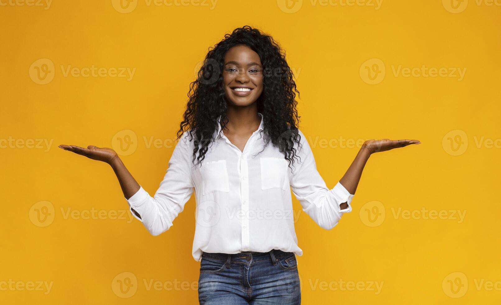 Make right choice. Positive african girl comparing variants, making scales with his empty hands, yellow studio background, free space photo