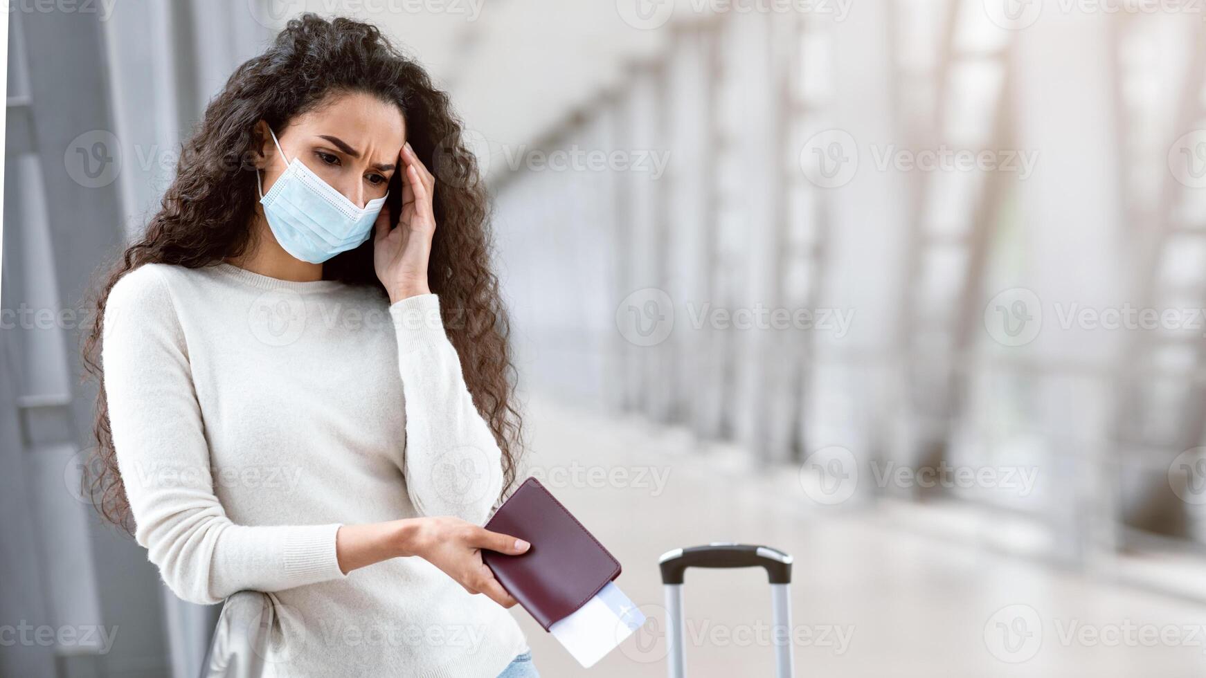 Flight Cancellation. Upset Young Woman Wearing Medical Mask Waiting At Airport, Frustrated Female Holding Passport And Tickets While Standing At Terminal With Sad Face Expression, Copy Space photo
