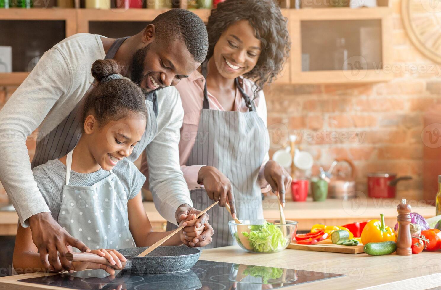 Kind afro parents teaching their adorable daughter how to cook healthy food in kitchen, copy space photo
