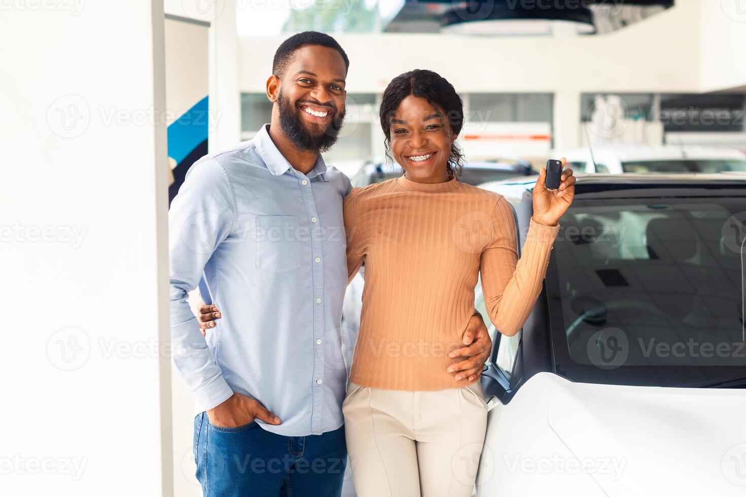 Happy Owners. Joyful African American Couple Posing With Car Keys In Hands In Dealership Center, Portrait Of Young Black Spouses Celebrating Buying New Automobile In Modern Showroom, Copy Space photo
