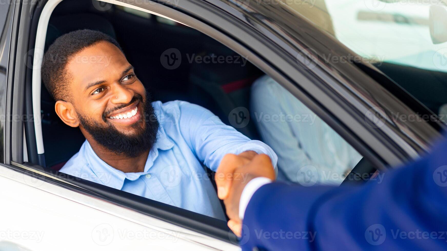 Black Male Customer Sitting Inside Of His New Car And Shaking Hands With Salesman After Buying Own Automobile In Modern Dealership Center, Salesperson Greeting Happy African American Man, Closeup photo