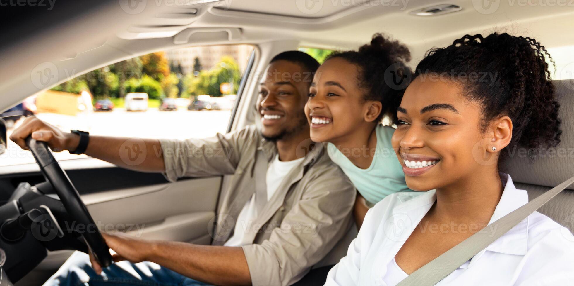 Happy Black Parents And Daughter Riding A Car Smiling Looking Aside Sitting In Seats Enjoying Road Trip By Auto. Automobile Tourism, Traffic And Transportation Concept. Side View, Selective Focus photo