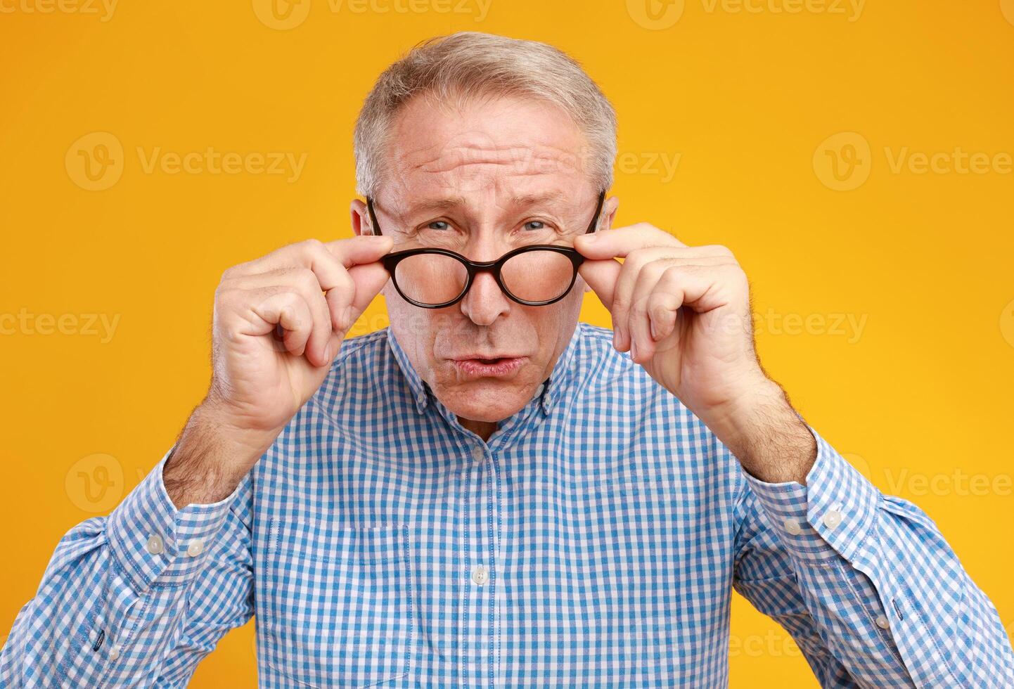 Poor Eyesight. Senior Man Can't See, Squinting Eyes Wearing Eyeglasses Having Problems With Vision, Looking At Camera, Yellow Orange Wall. Ophtalmic Issue In Older Age, Macular Degeneration Concept photo