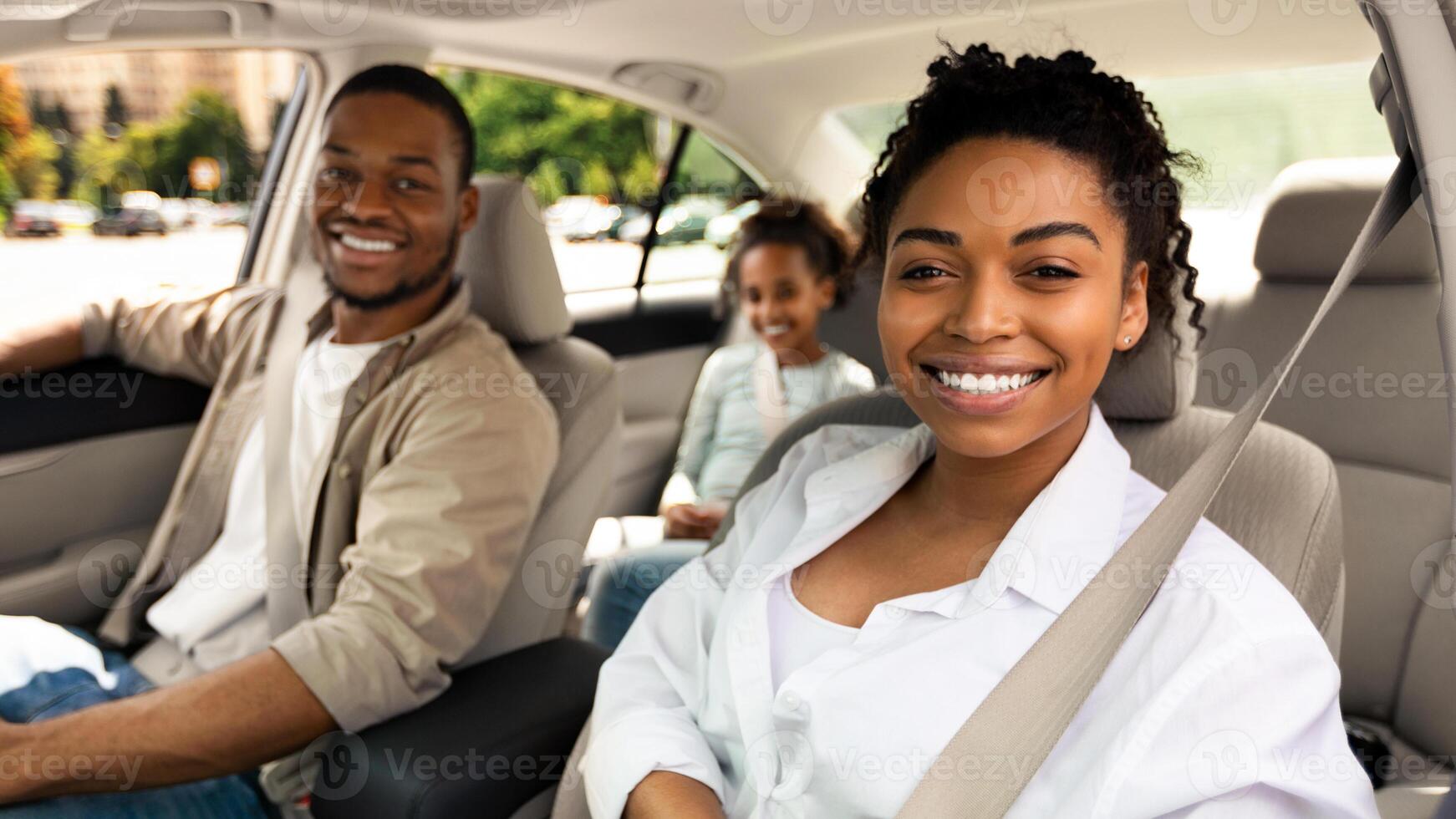Happy Family In Car Smiling To Camera Sitting In Seats Having Ride Across City. Parents And Daughter Driving New Automobile Travelling On Summer Vacation. Selective Focus photo