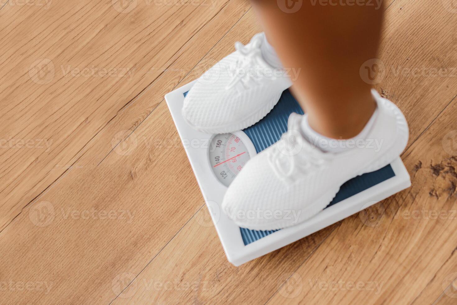 Closeup above top view of young sporty woman standing on scales indoors, checking her weight and results. Unrecognizable lady on slimming diet. Vertical cropped shot, high angle photo
