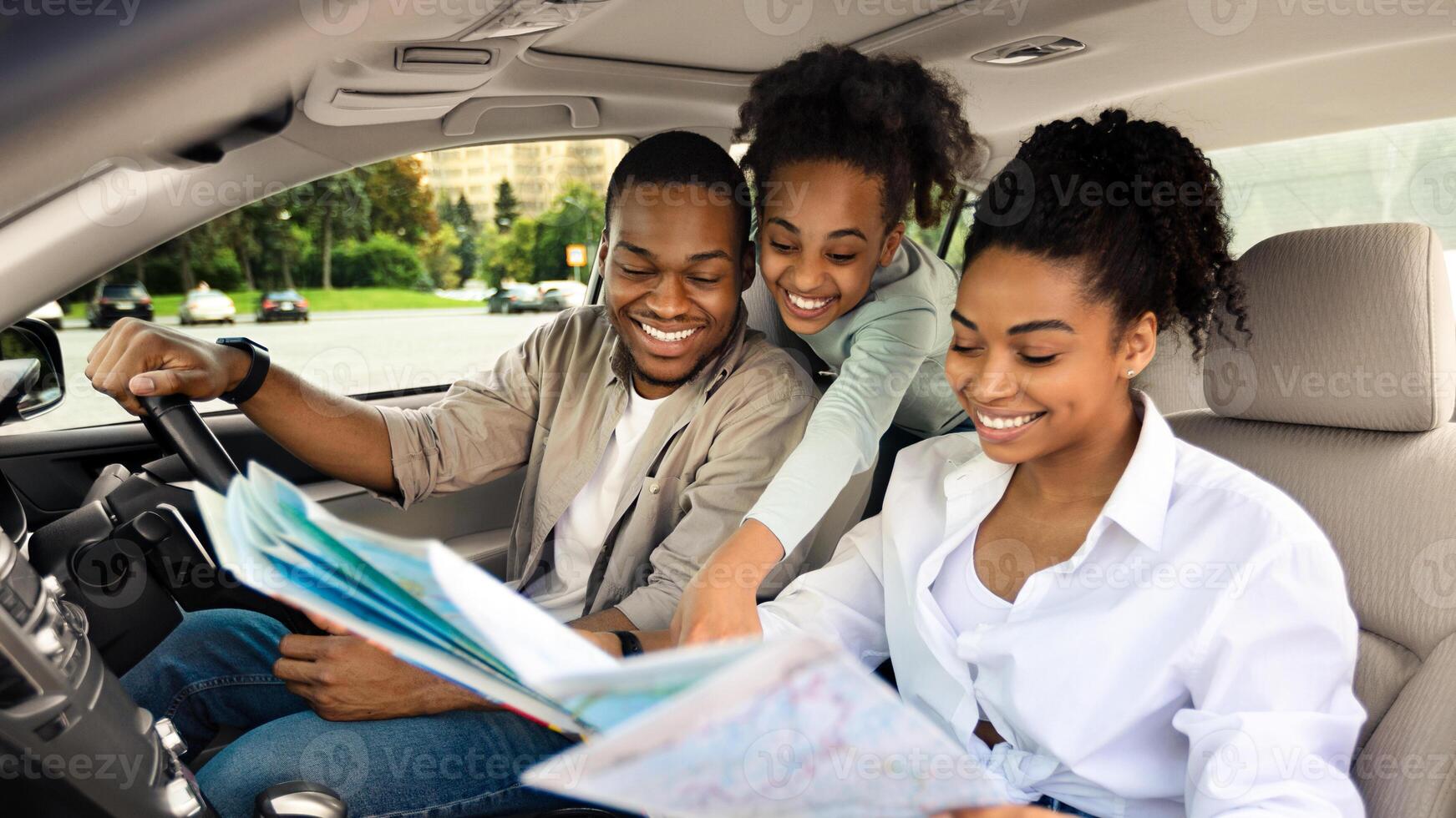 Happy African American Parents And Daughter Sitting In Car Holding Map For Navigation, Planning Summer Road Trip. Family Enjoying Auto Tourism Traveling Together On Vacation photo