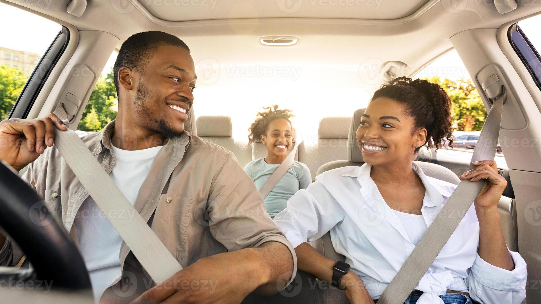 Joyful Black Family Riding New Car Enjoying Summer Road Trip Together. Parents And Little Daughter Sitting In Automobile, Putting On Seat Belts For Safety. Transportation, New Auto Concept photo