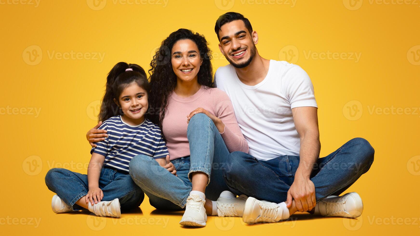 Portrait Of Happy Young Middle Eastern Family Of Three With Little Daughter Posing Together In Studio, Cheerful Arab Parents And Cute Child Sitting On Floor And Smiling At Camera, Free Space photo