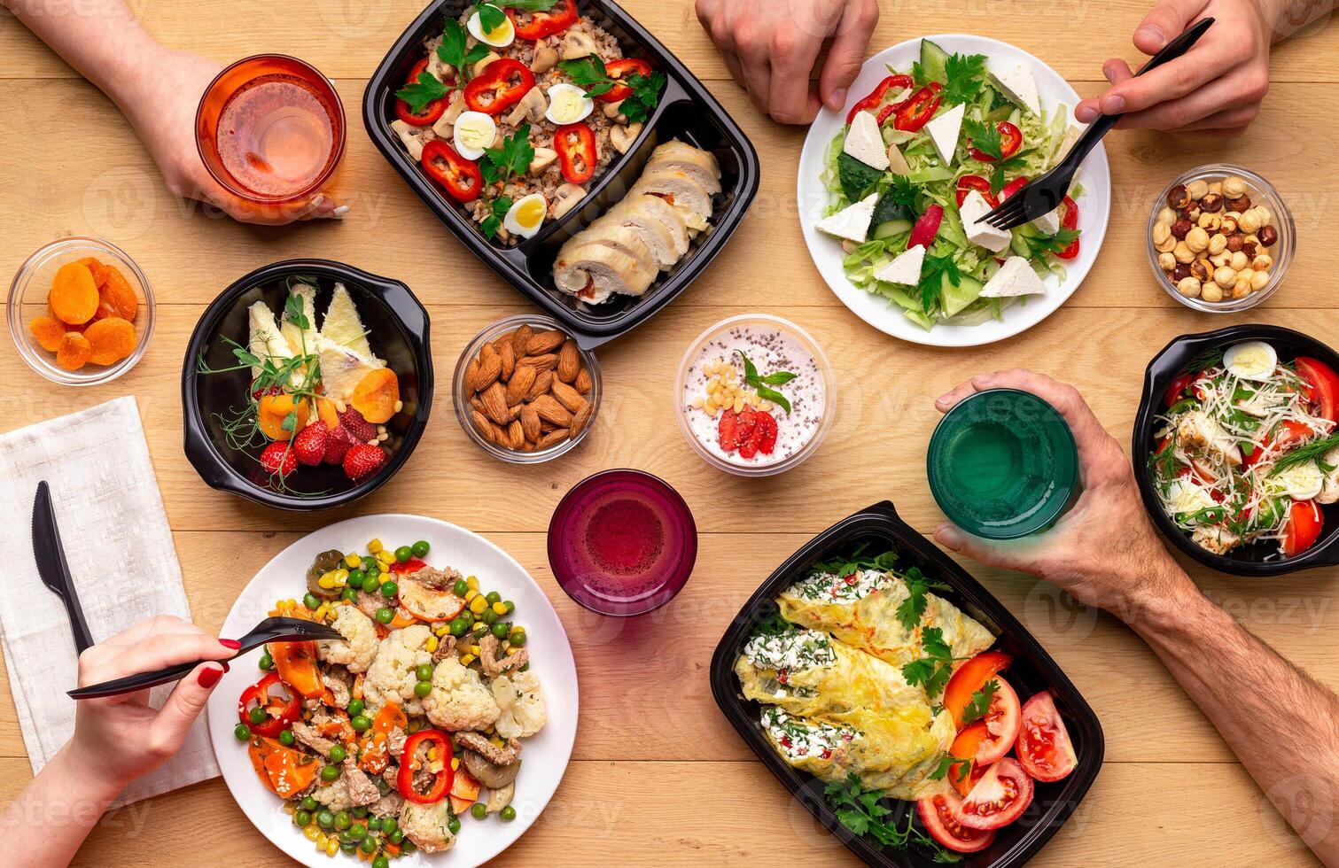 Lunch breack in modern office. Four people eating healthy meals from take away lunch boxes and plates at wooden table. concept, top view photo