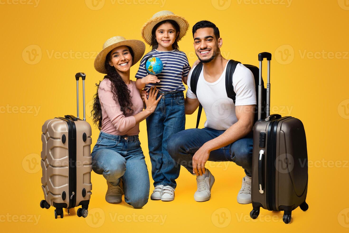 Family Travel. Cheerful Arab Parents And Little Daughter With Suitcases Posing Together Over Yellow Background, Happy Middle Eastern Girl Holding Small World Globe, Ready For Trip With Mom And Dad photo