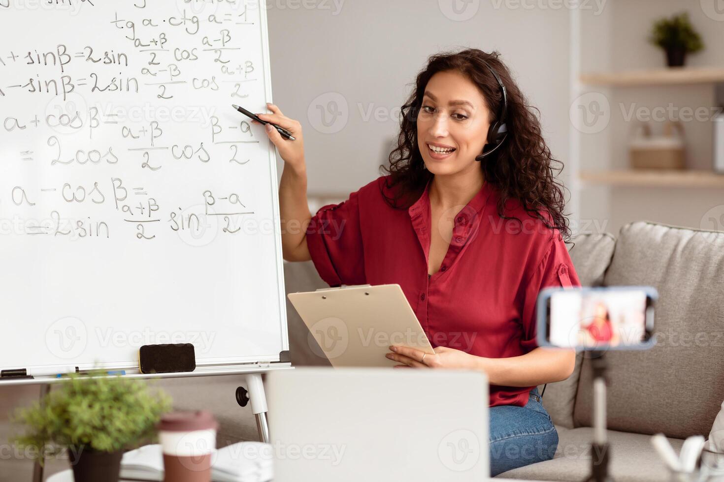 Studying Online During Covid-19 Pandemic. Smiling lady math teacher in headphones giving lesson on web, using smartphone and pc. Millennial lecturer having call with students recording vlog photo