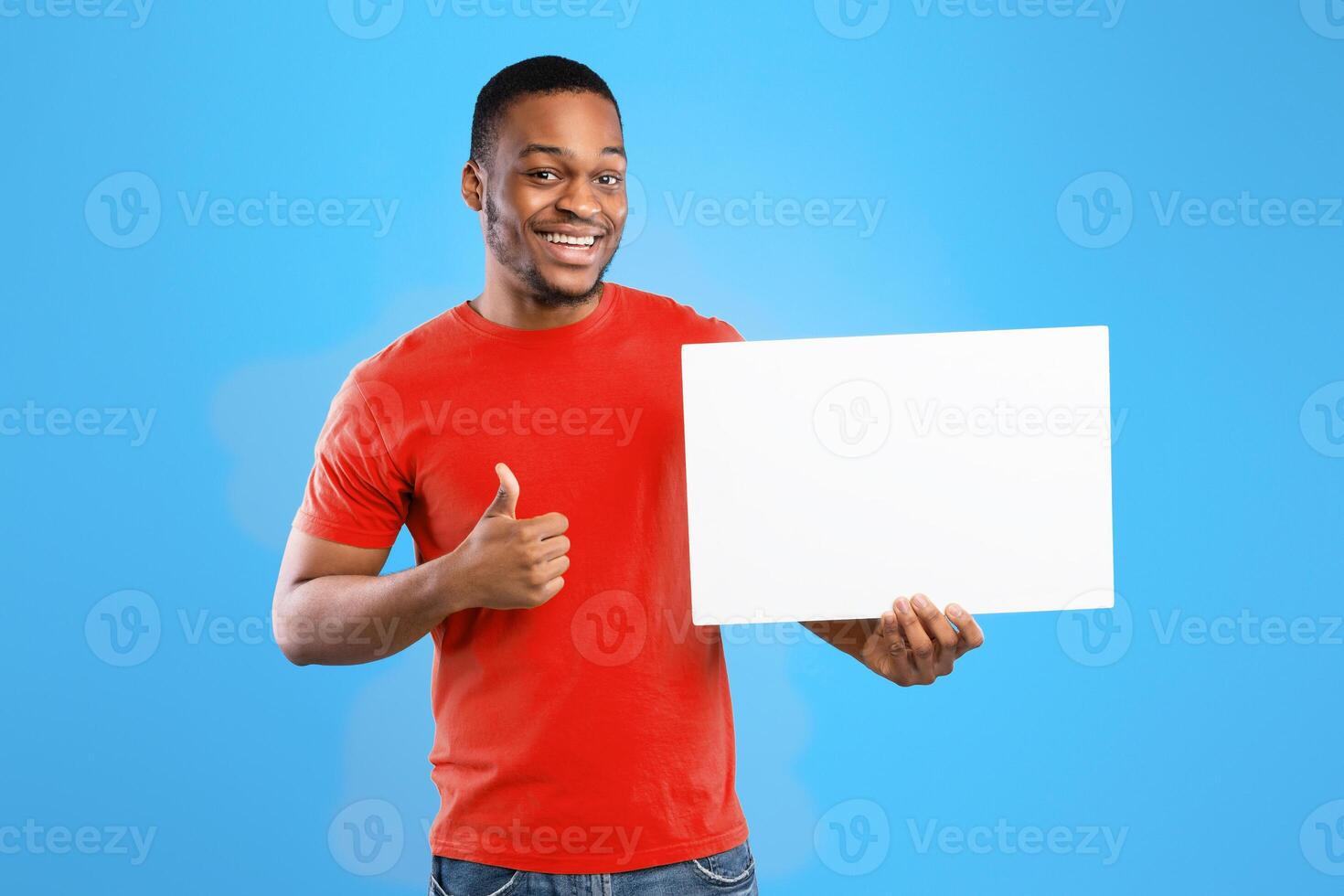 Great Offer. Cheerful Black Guy Showing Blank White Board For Your Text And Gesturing Thumbs Up Over Blue Studio Background. Advertisement Banner With Man Holding Empty Poster. Mockup photo