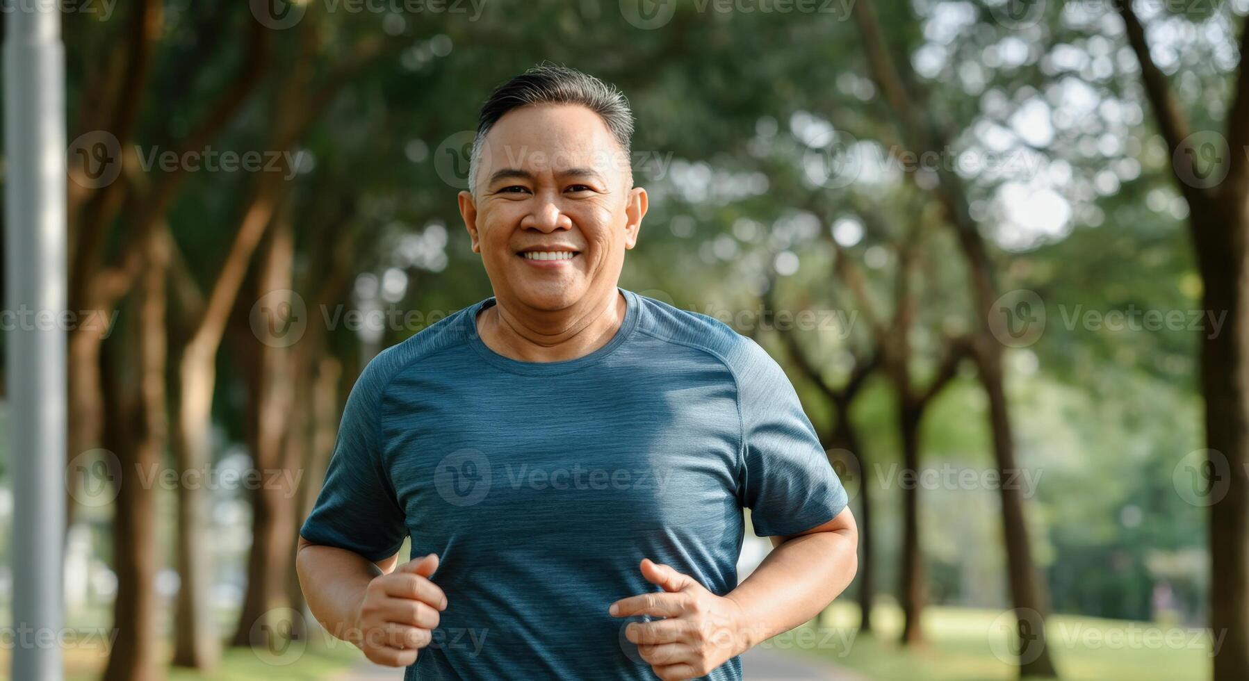 Mature asian man in blue running outdoors in scenic park setting photo