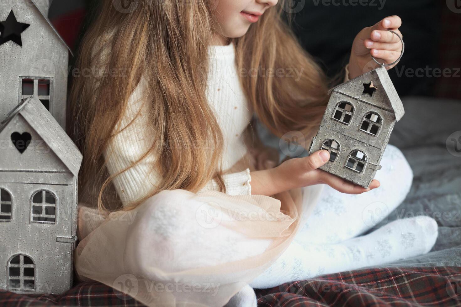 Young girl engaged in creative play with decorative toy houses on cozy bed photo