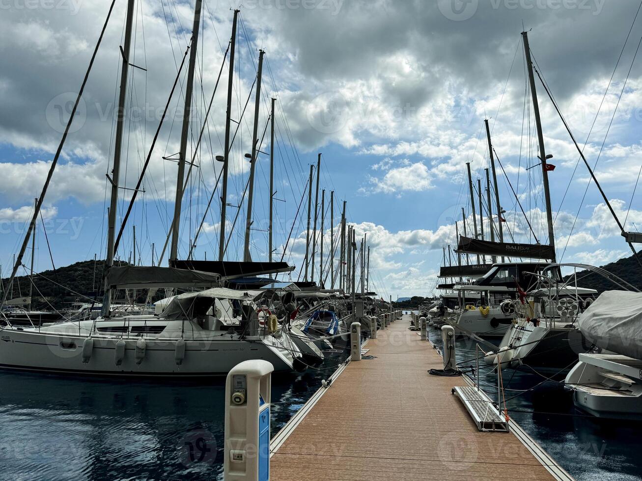 Calm marina with sailboats docked under a partly cloudy sky in a serene setting photo
