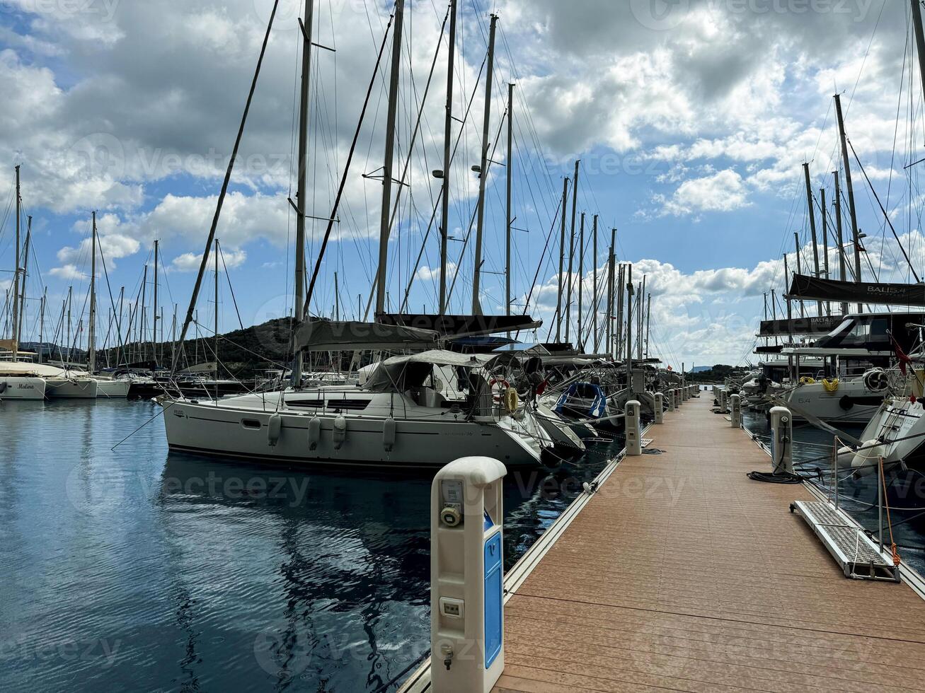 Sailboats docked in a sunny marina with clear blue skies and scattered clouds photo