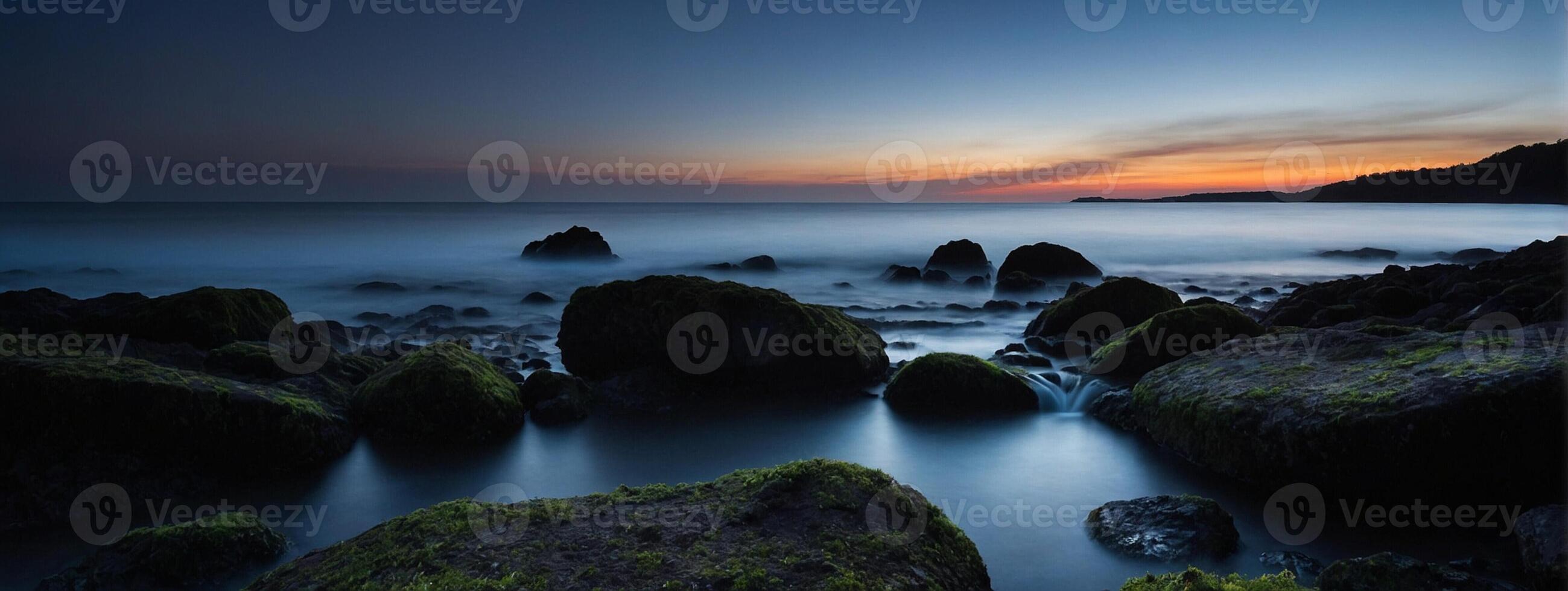 A sunset over the ocean with rocks and water photo