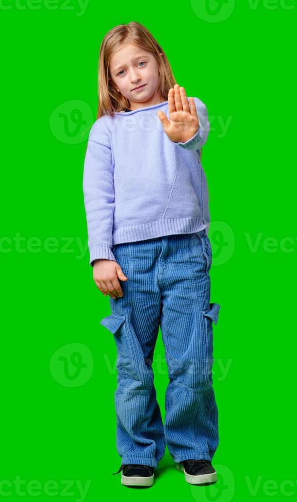 A young girl in a light purple sweater poses with her hand extended, signaling a stop gesture against green background photo
