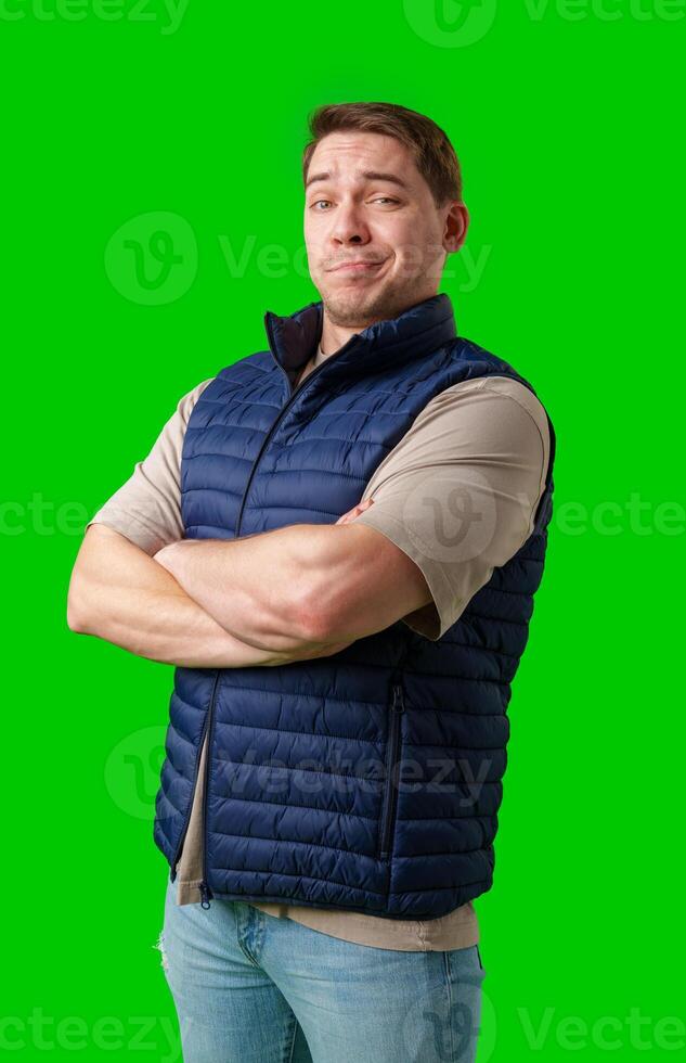 Confident man in a navy vest and t-shirt poses with crossed arms against a bright green background photo