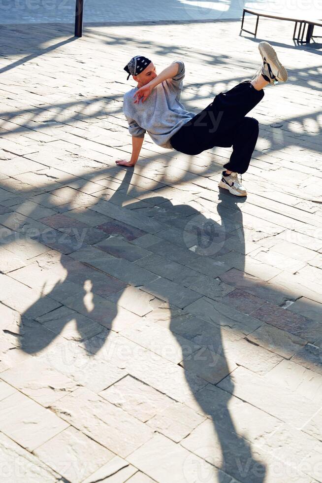 A young man performs a dance move on a tiled street during the day photo